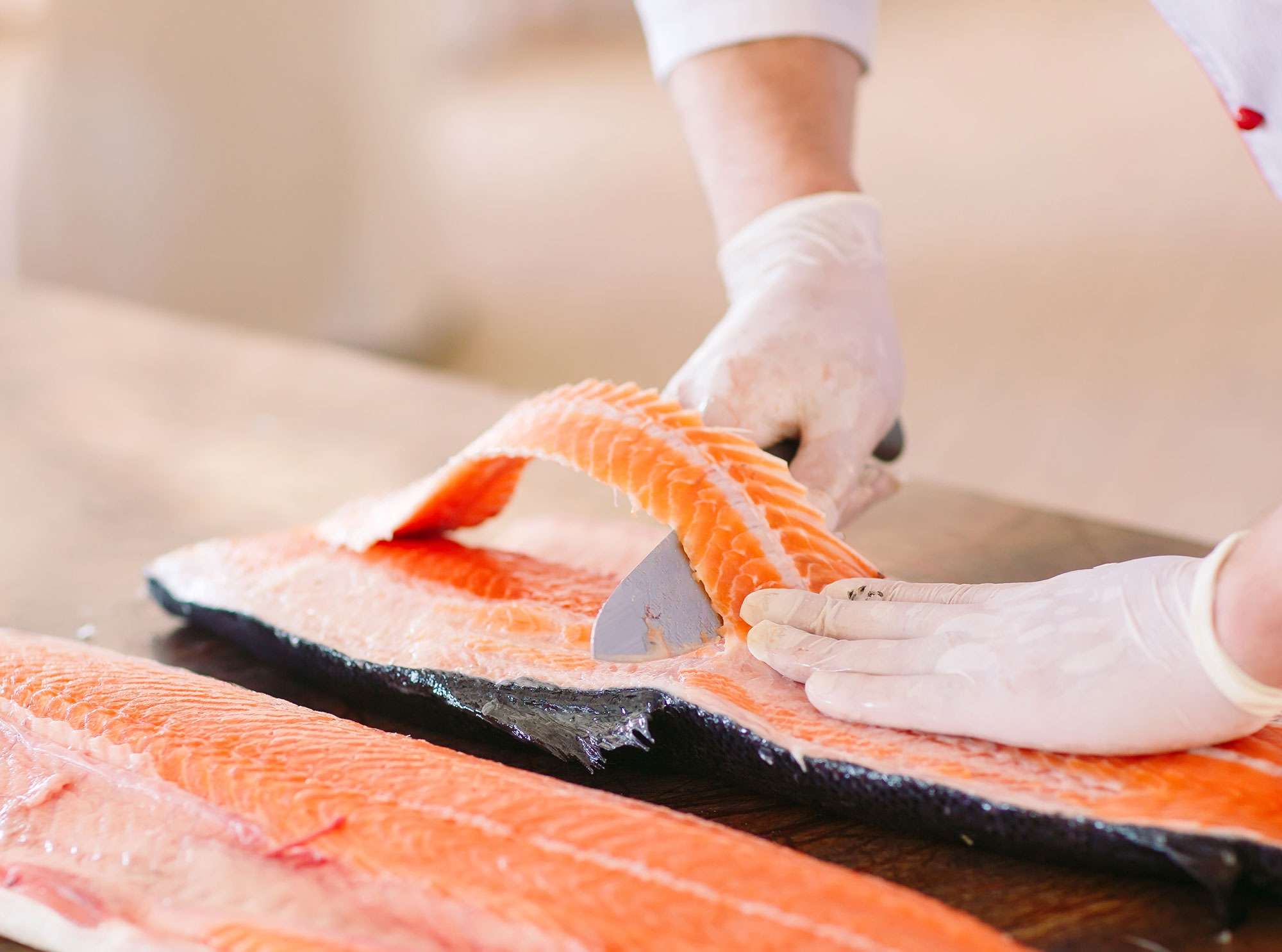 A close up of gloved hands deboning raw salmon fillet