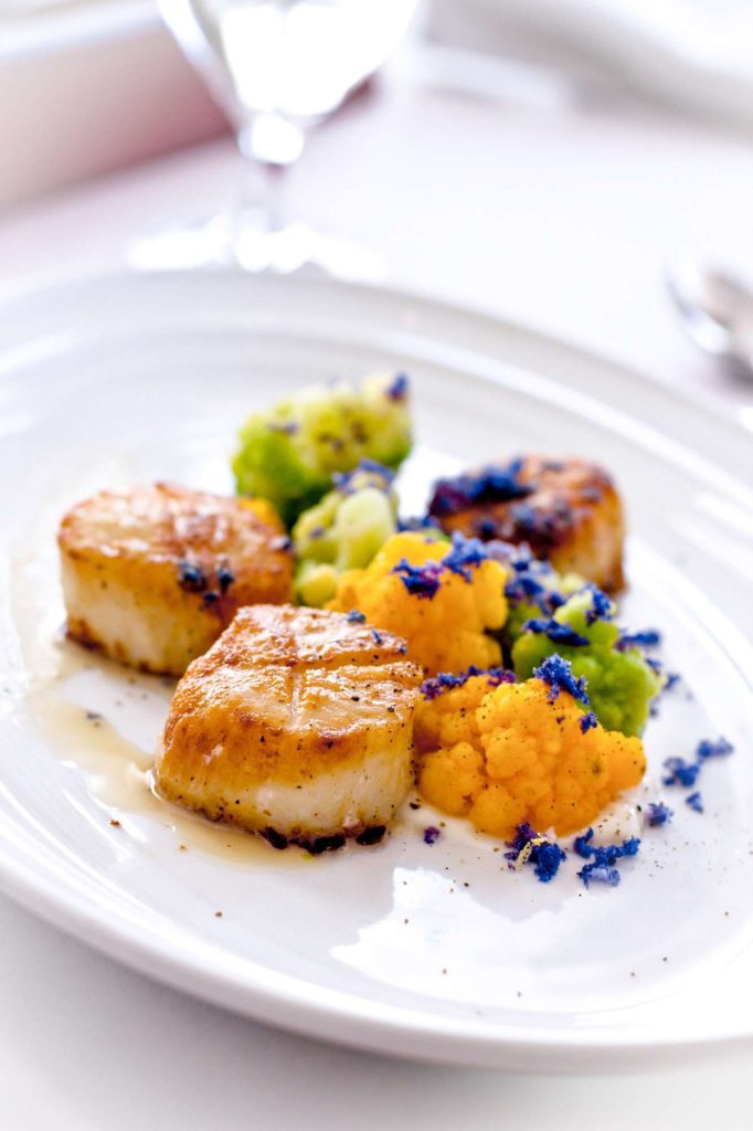 A photo of plated delicious scallops with colorful garnish.