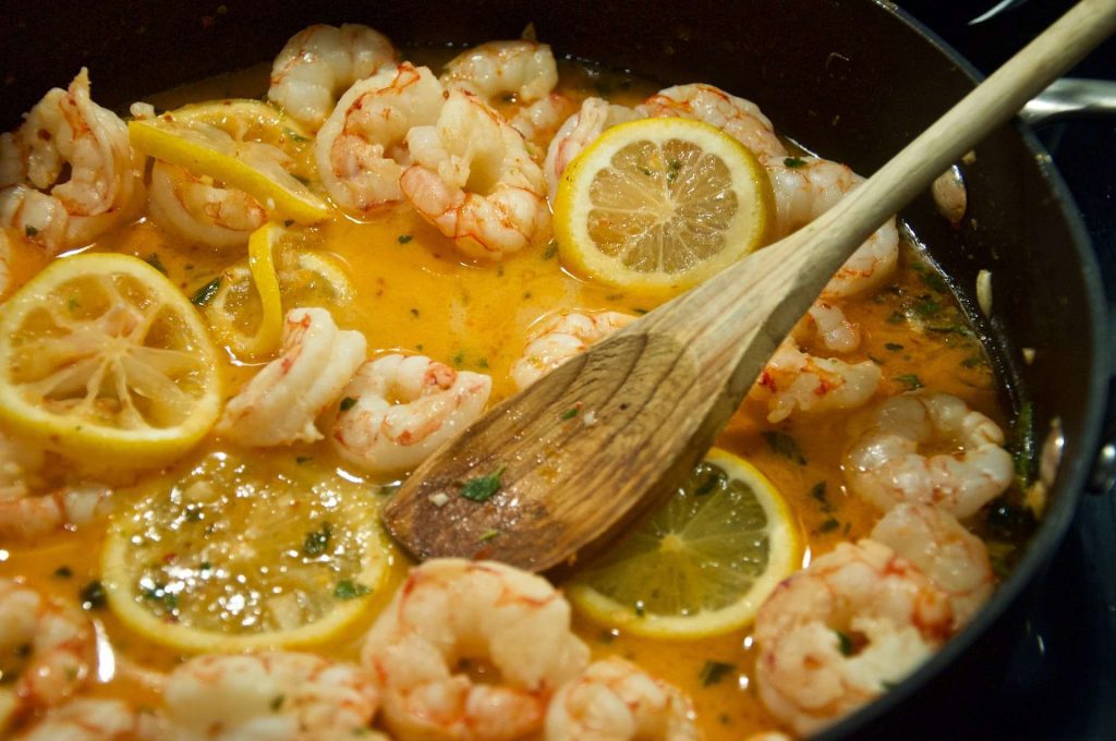 Shrimp and lemon smothered in butter cooking in cast iron pan.